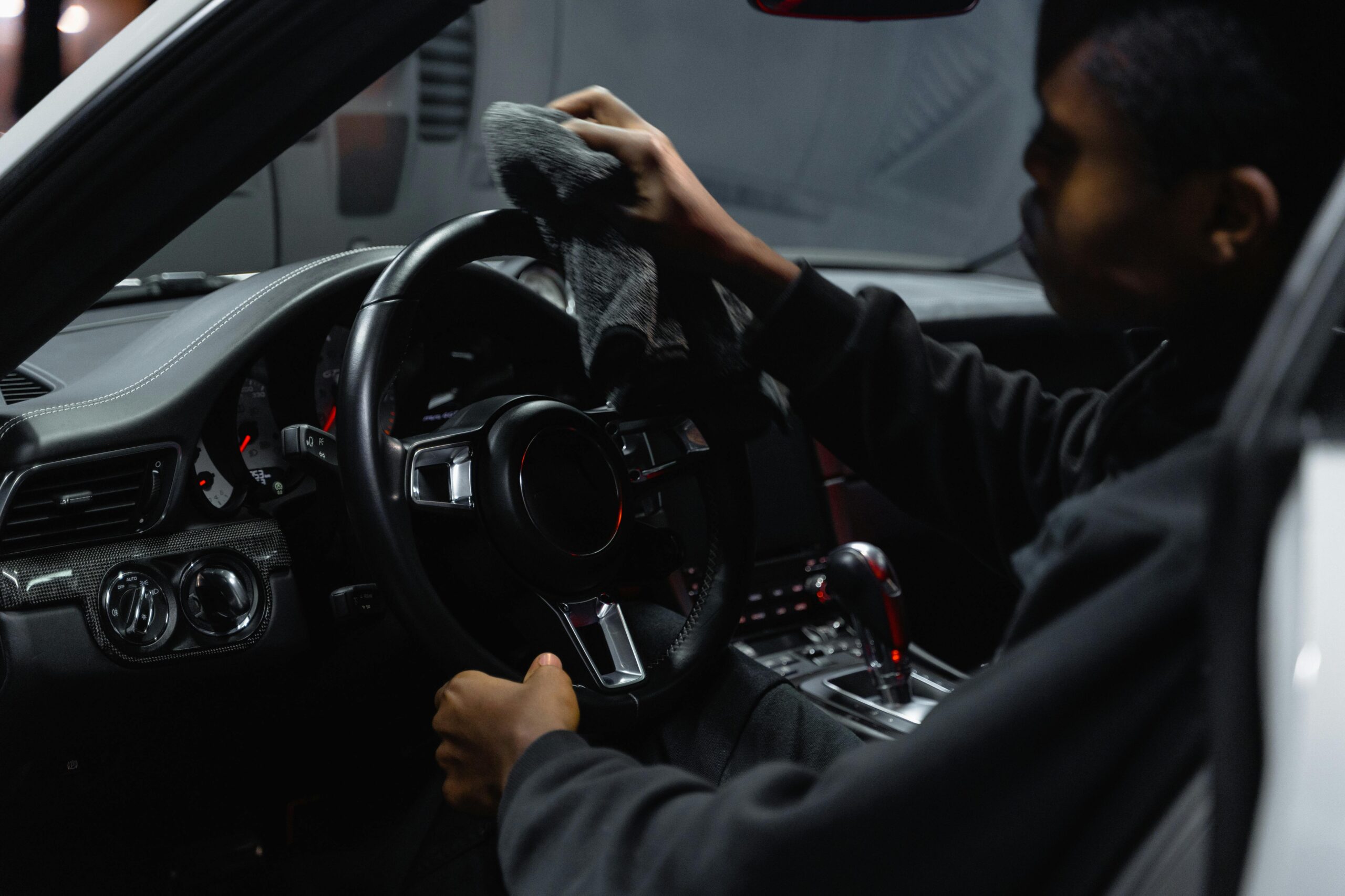 Adult man wiping a car steering wheel with a cloth inside a vehicle.